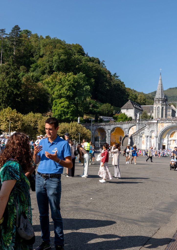 Séminariste aidant un pèlerin sur l'esplanade du Rosaire